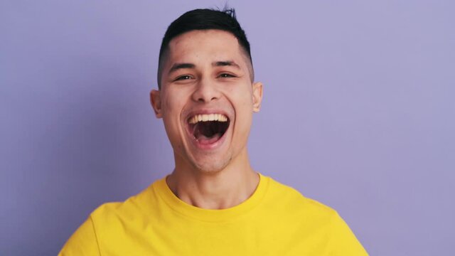 The positively surprised man screaming and making a winner gesture while standing in the purple studio