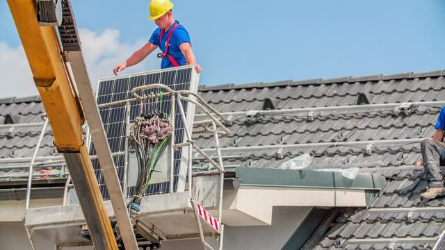 Slow motion track shot showing male worker lifting solar panel on roof for installation.