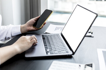 A woman holding a smartphone and using a laptop uses a smartphone. Chat with friends through instant messaging to discuss business together and use your laptop to find information on the web.