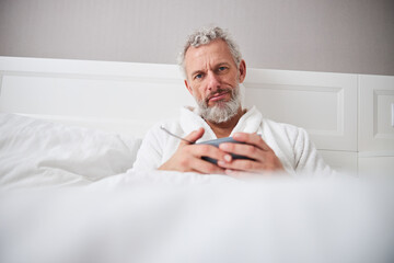 Sad adult handsome man posing and looking at the photo camera in bedroom