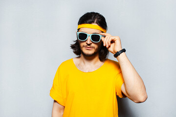 Portrait of young man wearing sunglasses and yellow shirt on grey background.