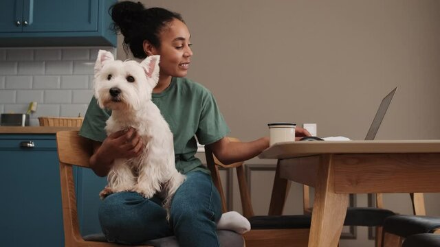 An attractive african american woman is petting the dog while sitting in the kitchen at home