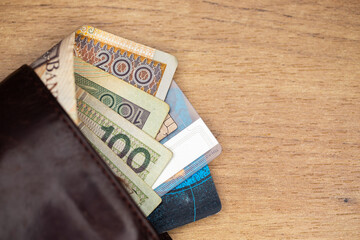 Lots of Polish banknotes and credit cards sticking out of a brown leather wallet. Photo taken under artificial, soft light