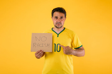 Brazilian soccer fan with yellow jersey and a sign that says 'No racism'