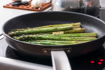 Seasonal asparagus frying in a pan with oilve oil on a stove top.