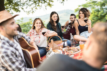 Group of people having fun eating and drinking wine at picnic party outdoor - Main focus on front girl faces