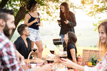 Group of people having fun eating and drinking wine at picnic party outdoors - Main focus on center faces