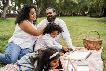 Happy indian family having fun painting with children outdoor at city park - Main focus on father...