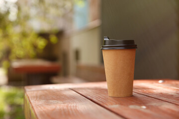 Takeaway paper coffee cup on wooden table outdoors, space for text