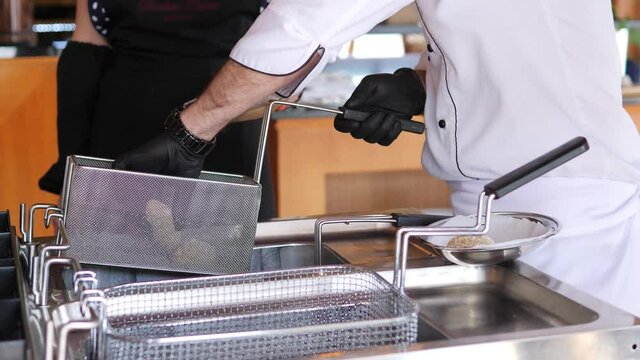 Close-up of a chef in black gloves putting a meat dish in a deep fryer.