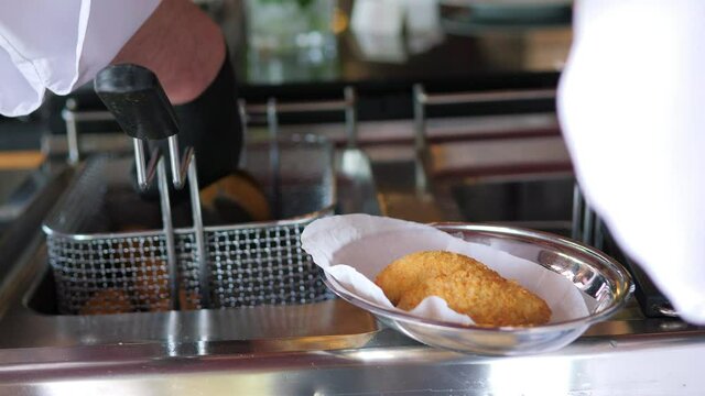 Close-up of a chef in black gloves putting a meat dish in a deep fryer.
