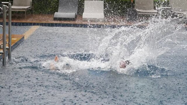 Man fall into water of swimming pool, clumsy swing hands and plop flat on back with big splash, slow motion shot. Heavy tropical shower, typical weather at Thailand in rainy season