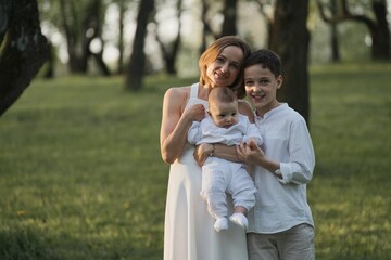 Fototapeta premium Mother and two children hugging. Happy family sitting outdoor: woman and two brother kids boys and cute little toddler boy