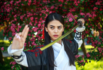 Young asian girl in traditional kimano in a blooming garden with samurai japanese sword katana in image of warrior woman