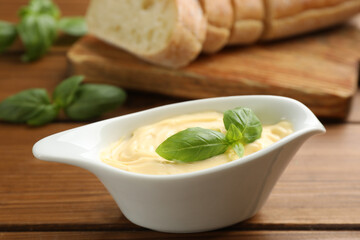 Tasty sauce with basil leaves in gravy boat on wooden table, closeup