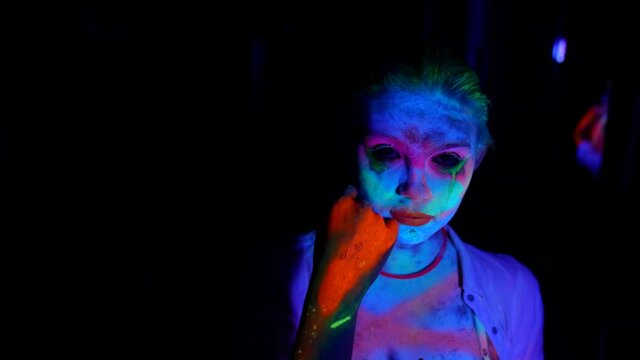 young actress with fluorescent makeup, medium portrait in UV lights in darkness