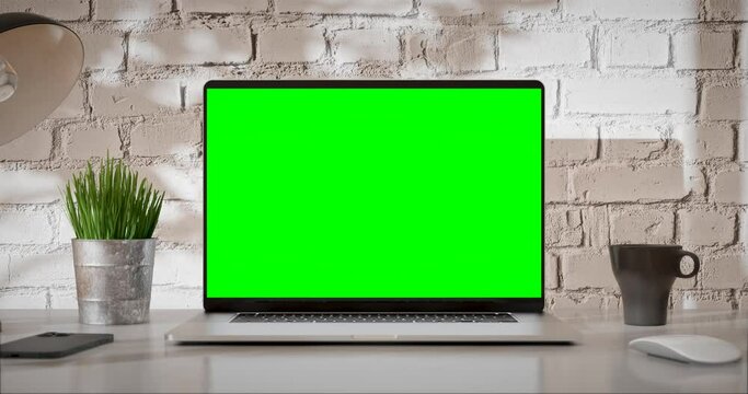 Laptop green screen is opening. Loft office interior with brick wall and swaying trees on the wind. The last 200 frames are looped