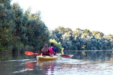Couple (man and woman) paddle a yellow kayak near trees at Danube river at summer