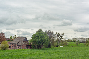 Fototapeta na wymiar Old farmhouse in a green hilly spring landscape with a cloudy sky.
