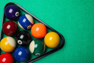 Plastic rack with billiard balls on green table, top view. Space for text