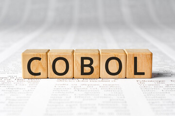 Cobol - word wooden blocks with letters, Cobol COmmon Business Oriented Language concept, paper background newspaper text
