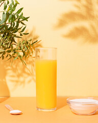 Orange juice glass and collagen powder on table with plant and shadow