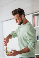 happy man preparing vegetable salad for breakfast in kitchen