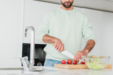 partial view of man preparing vegetable salad in kitchen on blurred foreground