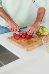 partial view of man cutting ripe cherry tomatoes in kitchen