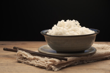 Cook Jasmine Rice in a bowl with wooden chopsticks on wood table with a black background.