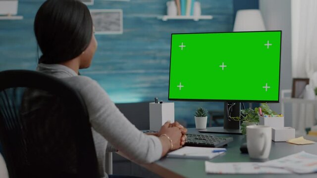 African american woman working remote from home listening school professor explaining online course. Student looking at mock up green screen chroma key display during virtual videocall meeting