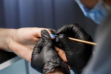 The master paints his nails with blue varnish. Manicure in a beauty salon