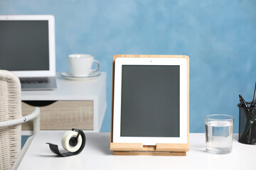 Modern tablet, glass of water and stationery on white desk