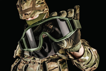 Photo of soldier in level 3 armored vest ammunition, tactical gloves holding tactical goggles on...