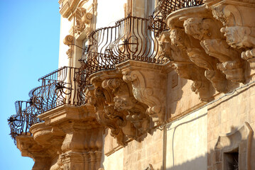 The beautiful balconies of Palazzo Trigona in Noto  with curved iron railings, corbels in carved...