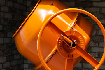 Close-up photo of orange colored concrete mixer standing on construciton sight.