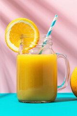 Orange juice in a glass with a straw and an orange on a colored background, close-up
