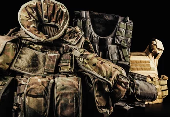 Foto op Canvas Various types of soldier camouflaged armored vests with shoulder and neck protection on black background laying on table. © breakermaximus