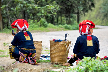 Hill tribe women waiting at the side of a dirt road in the countryside using mobile phone. Dressed...