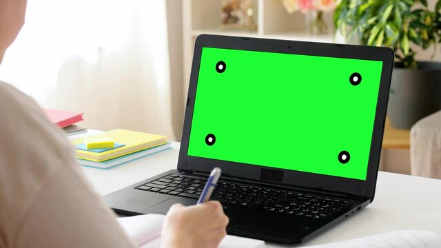 education, online school and distant learning concept - student woman with green screen on laptop computer, notebook and book at home