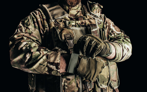 Photo of soldier in level 3 camouflaged armored vest putting on tactical gloves on black background. - Powered by Adobe