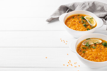 Masoor dal. Indian spicy red lentil soup in two white plates, gray napkin and dry raw lentil are on white wooden table.  copy space.
