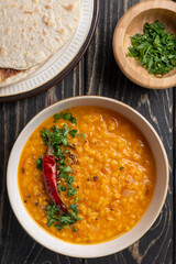 Masoor dal. Indian spicy red lentil soup, roti (chapati), sliced green coriander, are on brown wooden table.