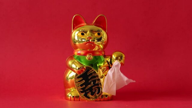 Golden Maneki-neko cat waving goodbye with tissue