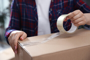 Woman taping cardboard box indoors, closeup. Moving day