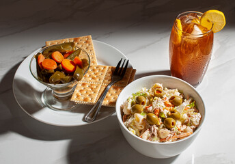 Tuna salad with elbow macaroni mayonnaise thin strips of carrots jalapeño or jalapeno chili and salted crackers and an ice tea on the saide over a white table, lit by the sunlight
