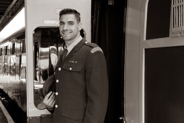 Handsome male british soldier in uniform standing next to train, smiling.