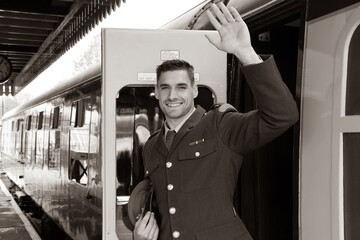 Handsome male british soldier in uniform standing next to train, waving and smiling.