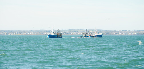 Two fishing boat, trawlers fishing Razor fish in an open Irish sea. Food industry, traditional craft, environmental damage concepts.