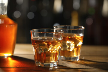 Glasses of whiskey with ice on wooden table in bar, space for text